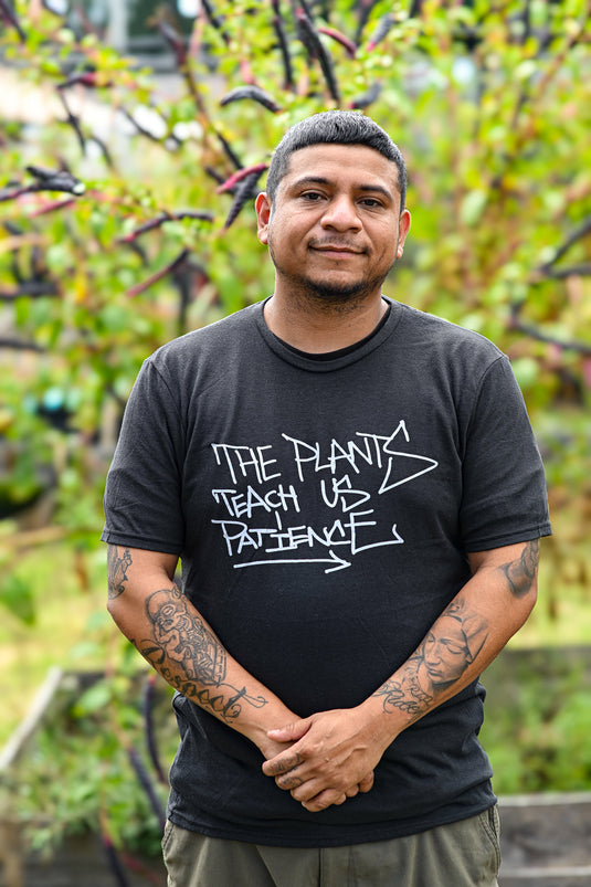 Man wearing a black t-shirt with text standing in front of greenery